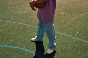Person holding a basketball on an outdoor court in casual attire.