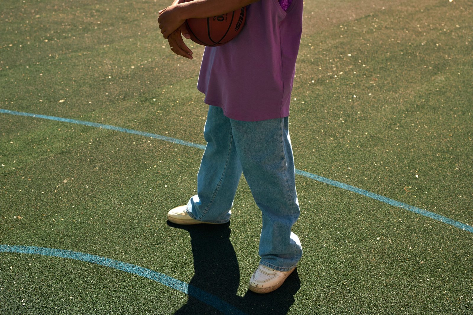 Person holding a basketball on an outdoor court in casual attire.