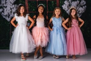 A cheerful group of girls in colorful dresses and crowns posing happily indoors.