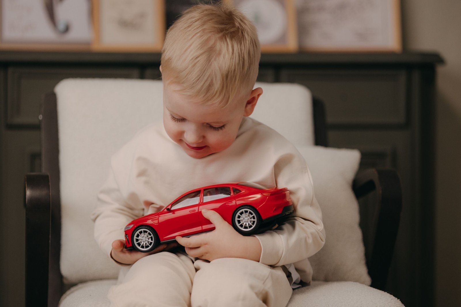 Adorable child playing with a red toy car while sitting indoors on an armchair.