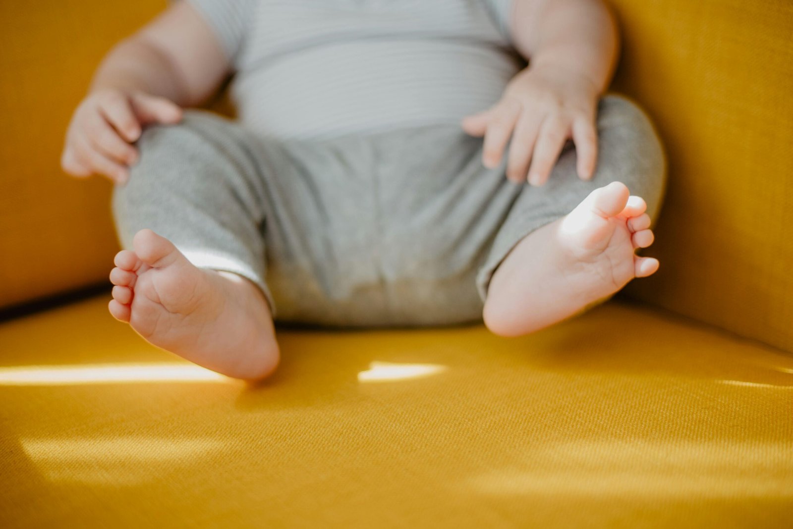 Cute baby feet and hands on a sunny yellow chair, evoking warmth and innocence.