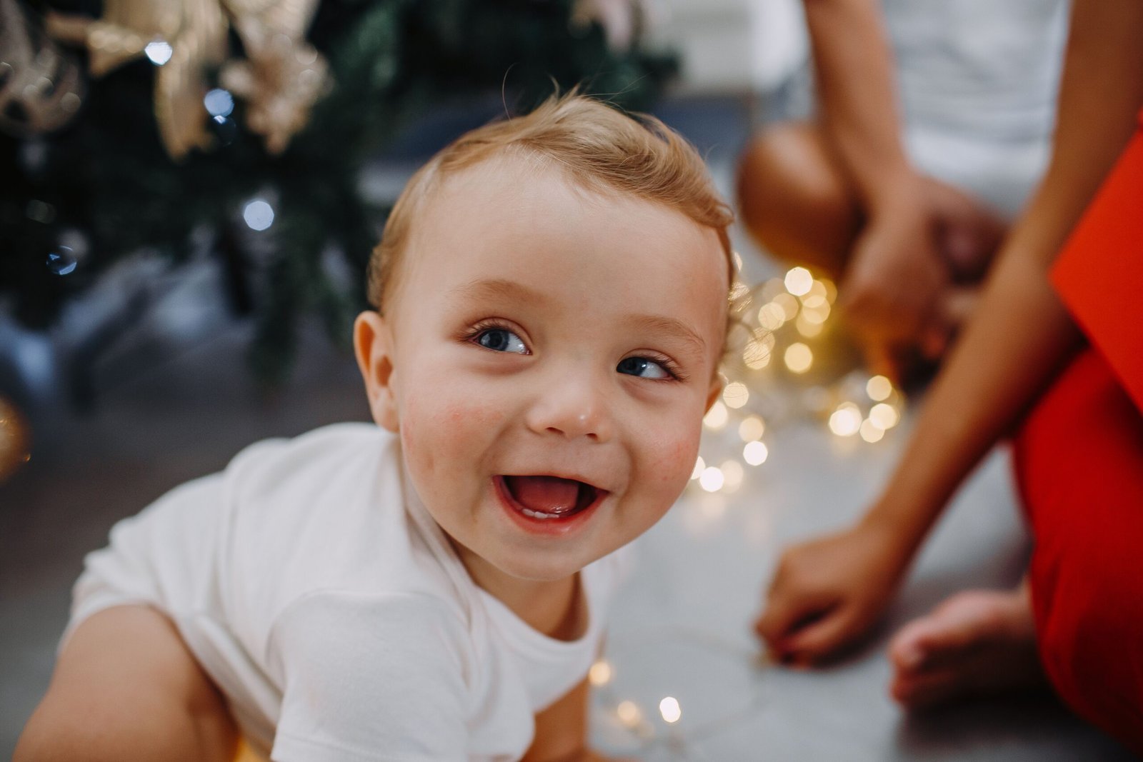 About Us A happy baby enjoying Christmas lights and holiday atmosphere indoors.