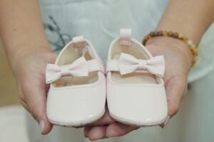 Adorable baby shoes with bows held in hands, perfect for a baby girl announcement or gift idea.