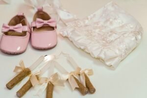 A collection of elegant baby christening accessories featuring pink shoes, a bonnet, and ribboned candles.