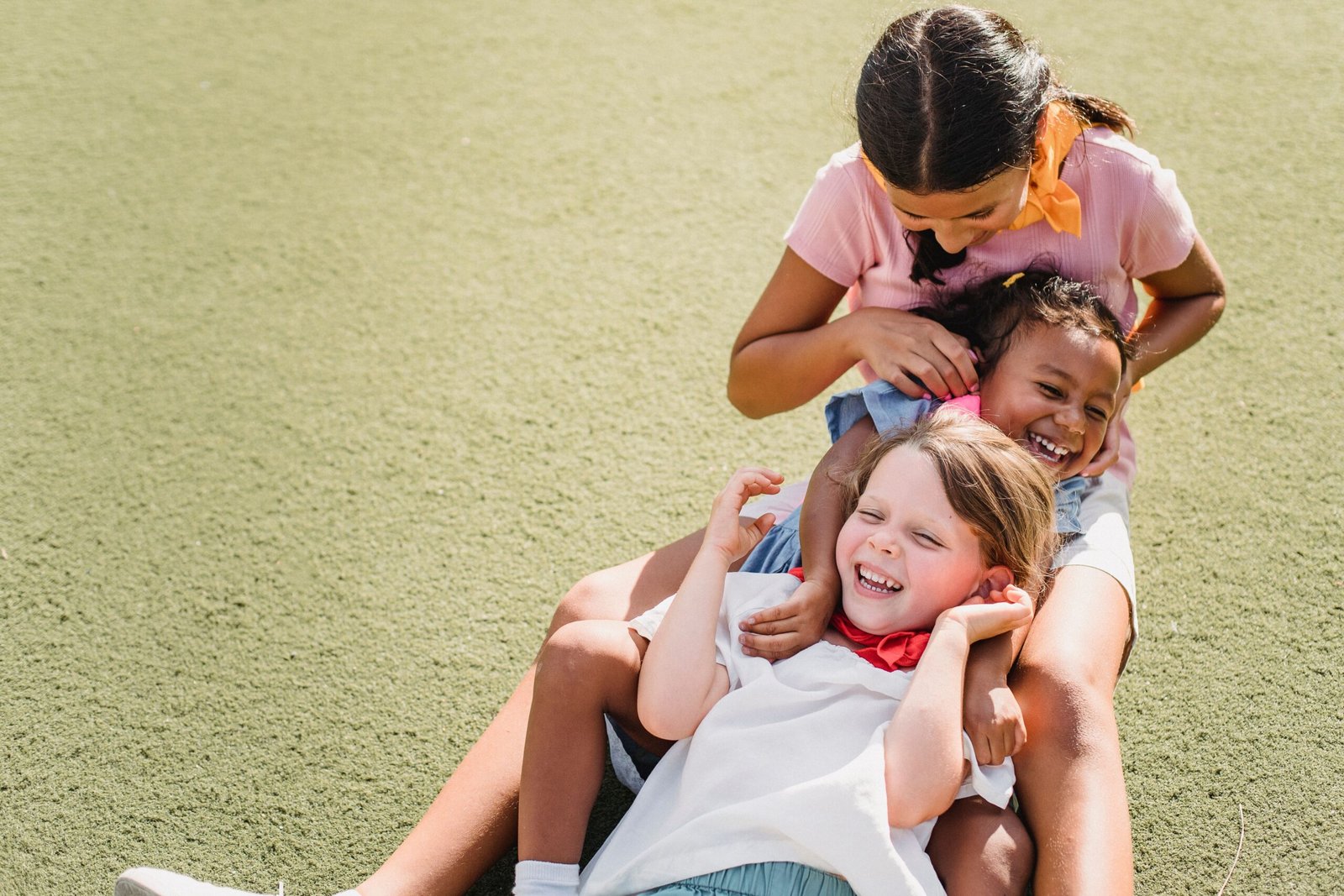 About Us Three children laughing and playing together on grass under the sunny sky, showcasing pure joy and friendship.