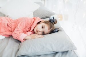 A young girl in a cozy pink robe lying comfortably on a bed with soft pillows.