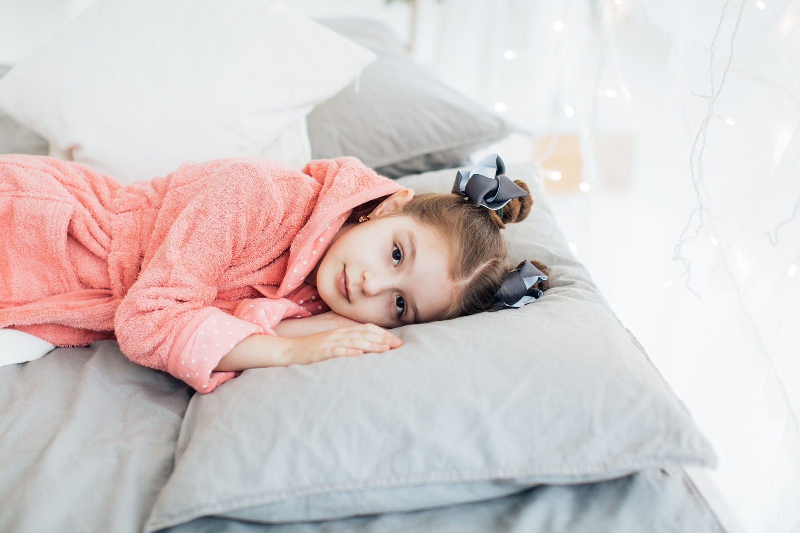 pexels photo 6202206 6202206 A young girl in a cozy pink robe lying comfortably on a bed with soft pillows.